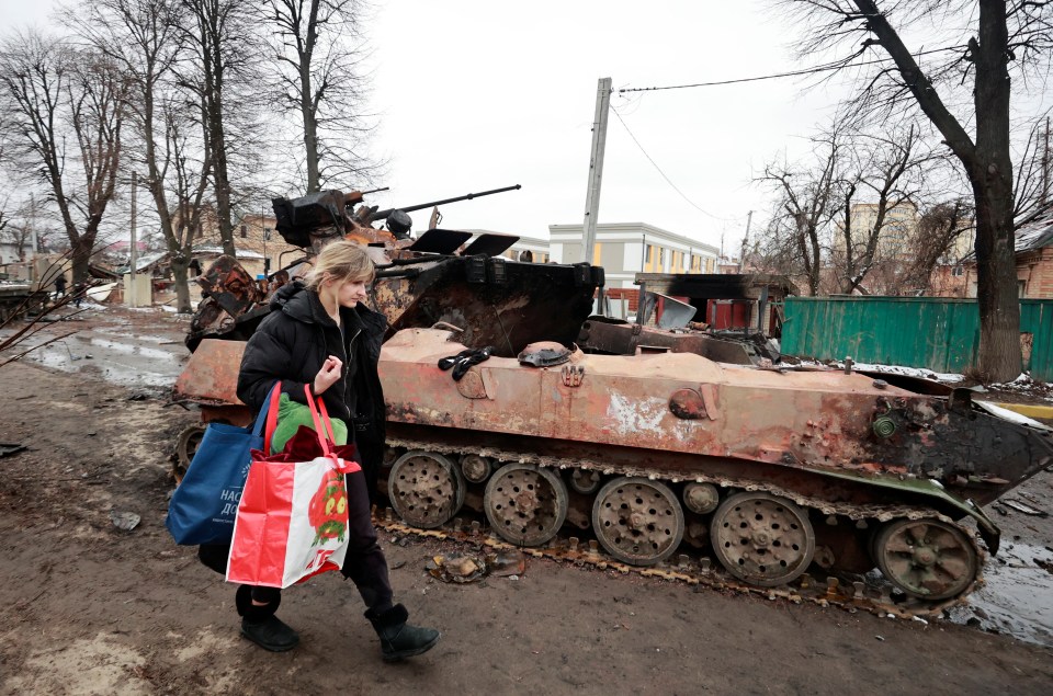 A woman walks past a destroyed military vehicle