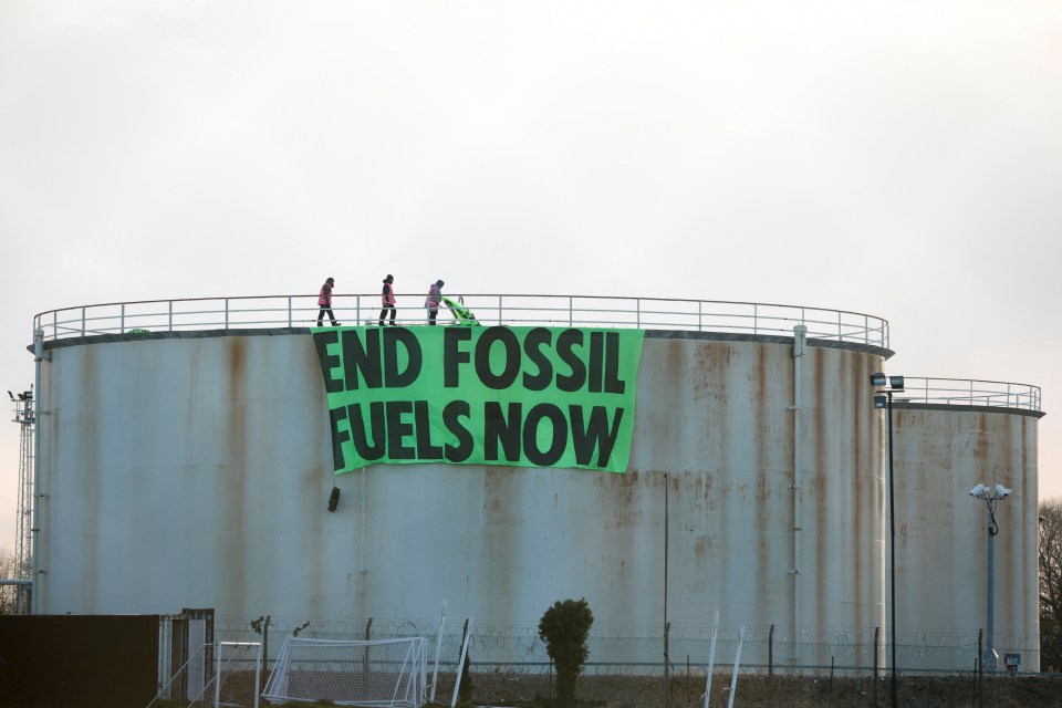 Extinction Rebellion activists hang a sign on a storage tank at Esso West London Terminal