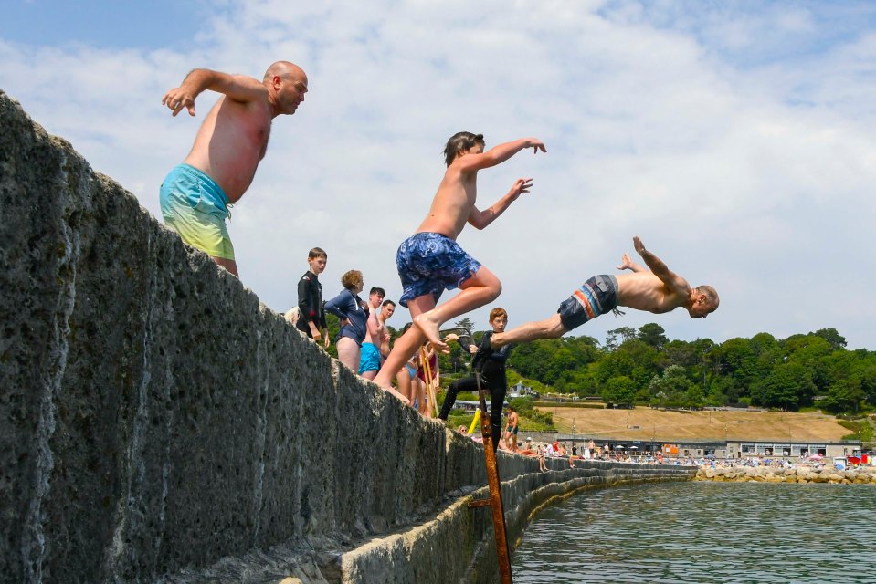 Kids leaping into the sea from the Cobb harbour wall in the Lyme Regis in Dorset