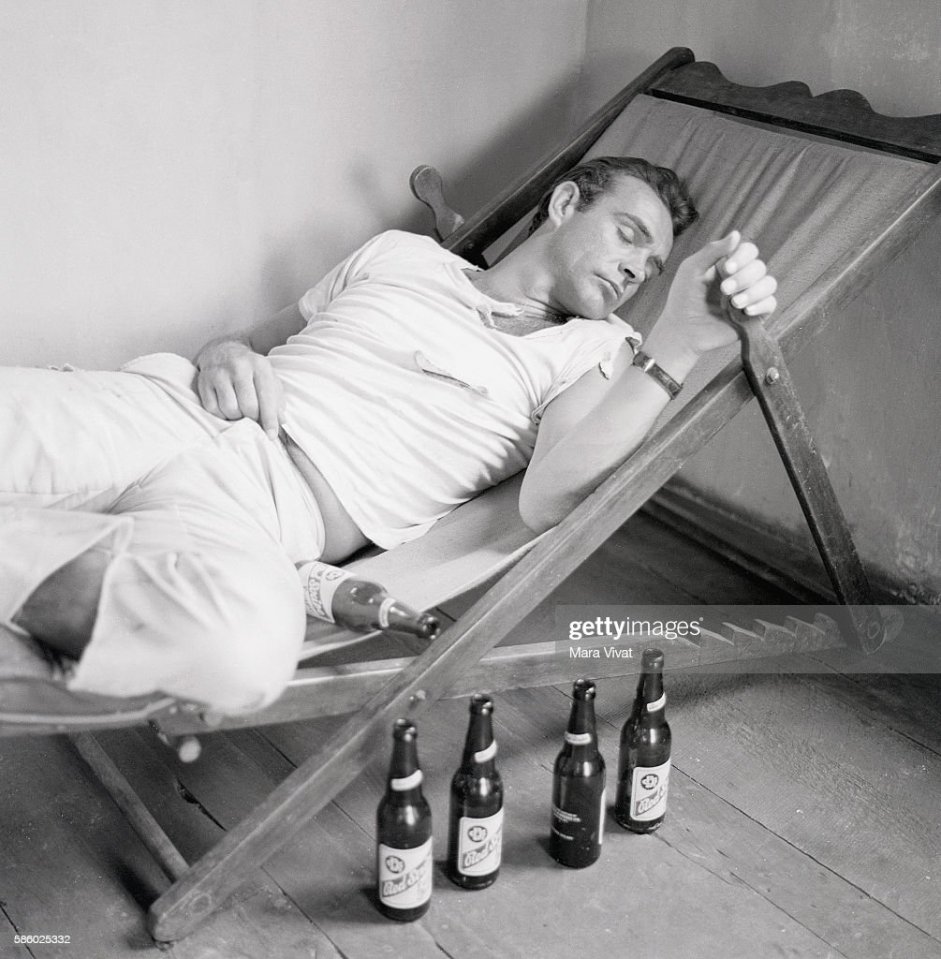Connery pictured asleep on a lounge chair beside a row of empty Red Stripe beer bottles
