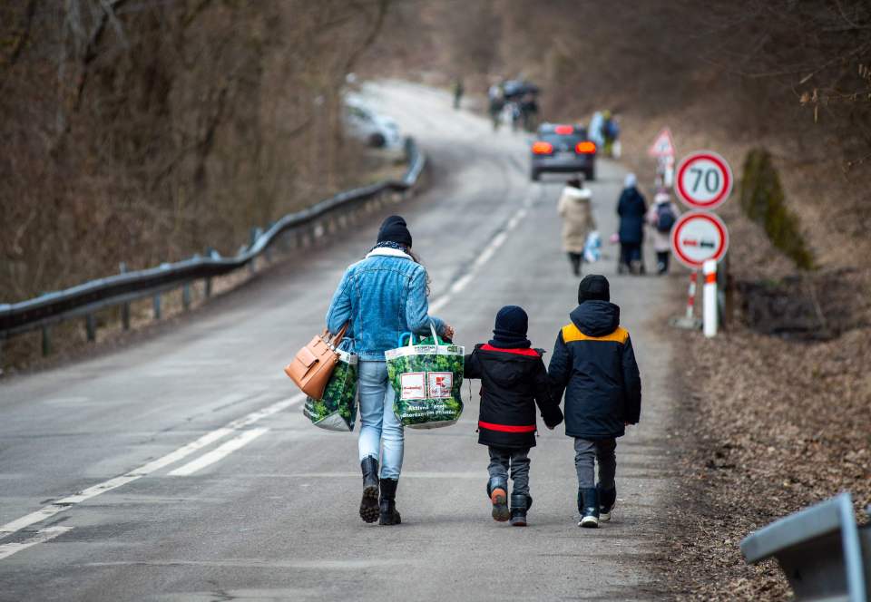 A woman with two children and carrying bags walk on a street to leave Ukraine after crossing the Slovak-Ukrainian border