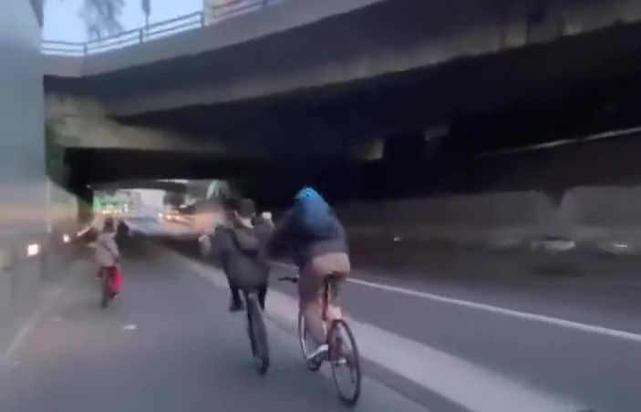 A man with a blue helmet and a backpack pushes the young man doing a wheelie