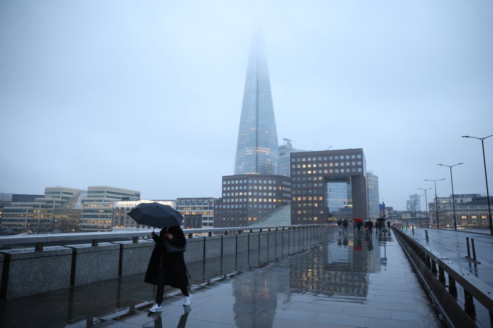 A pedestrian braves the rainy conditions as she walks across London Bridge in the capital this morning