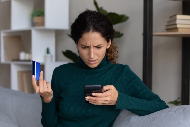 Worried woman looking at her phone and credit card after discovering an online scam.