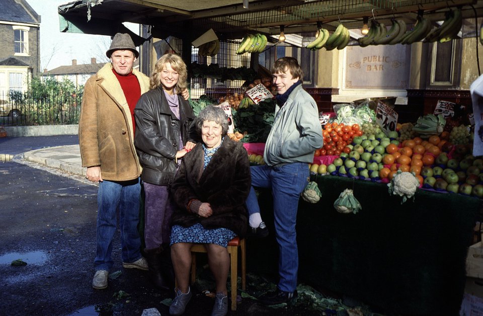 Photo of four actors from the TV show *EastEnders* at a fruit and vegetable stand.