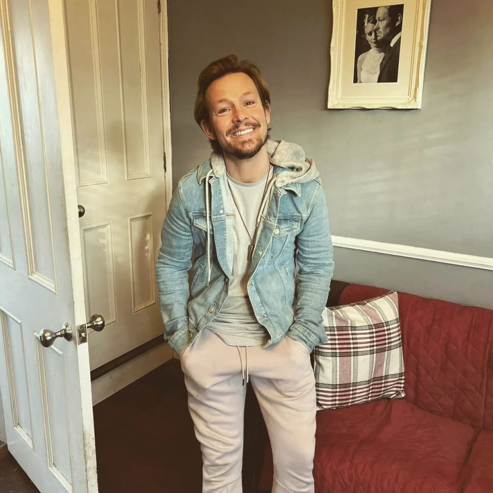 a man in a denim jacket stands next to a red couch