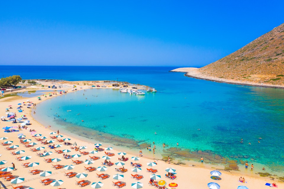 a beach with lots of chairs and umbrellas and boats in the water