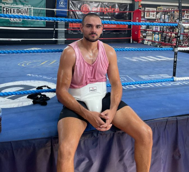 a man in a pink tank top sits in a boxing ring