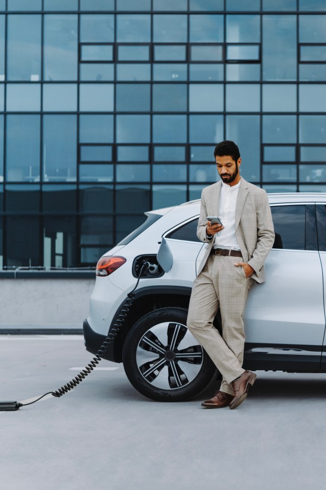 Young multiracial man using phone while waiting for car charging.