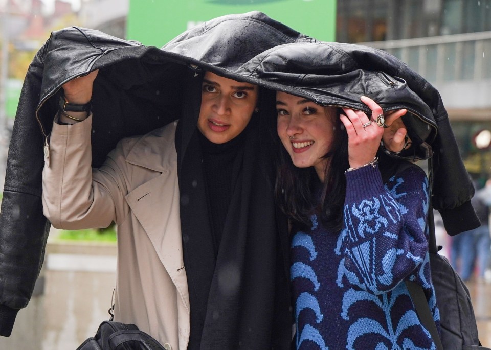 Shoppers shelter under their coats from the rain in Manchester
