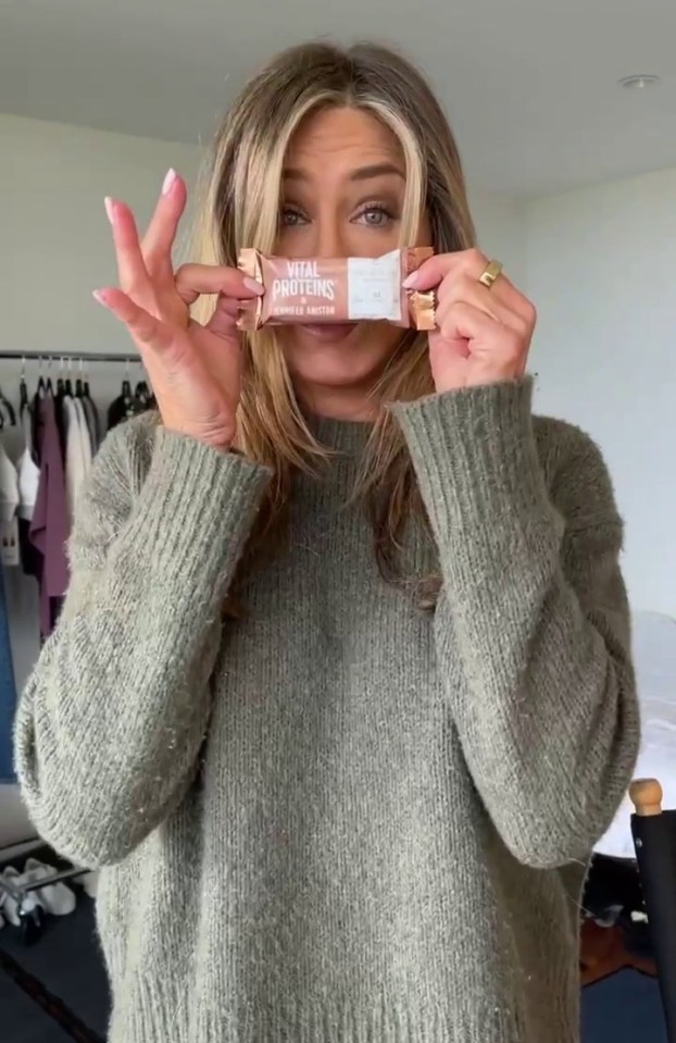 a woman in a green sweater is holding a vital proteins bar