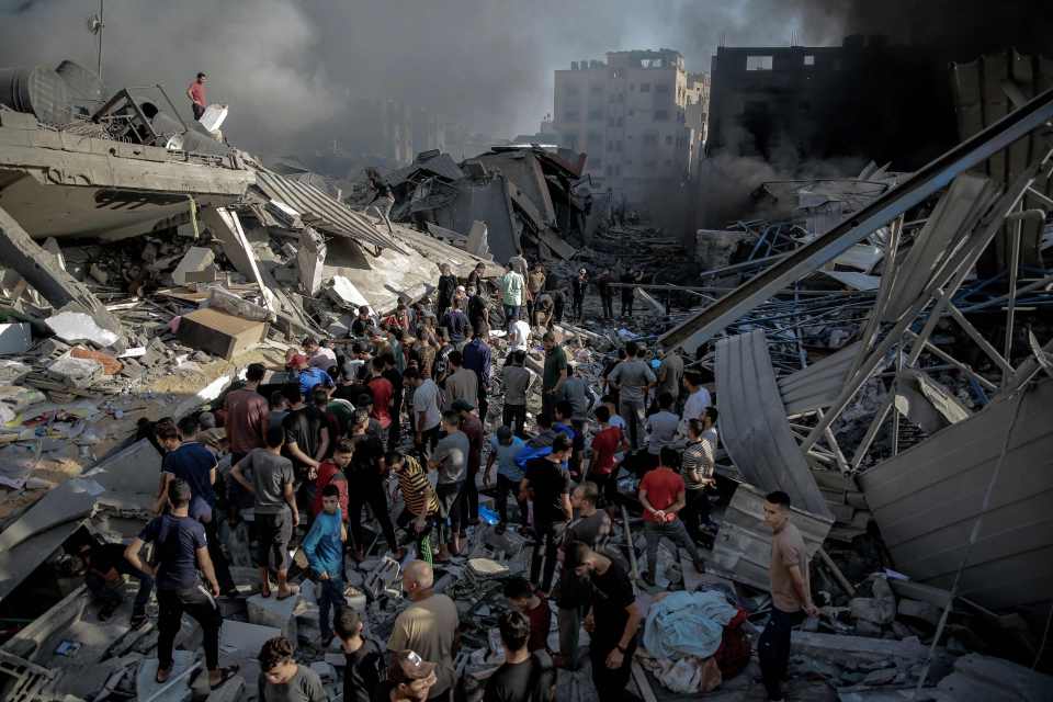 Smoke and fire rise from buildings as people gather amid the destruction in the aftermath of an Israeli strike
