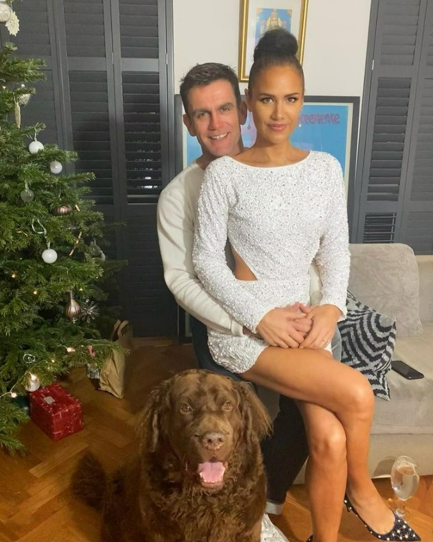 Couple posing with their dog in front of a Christmas tree.