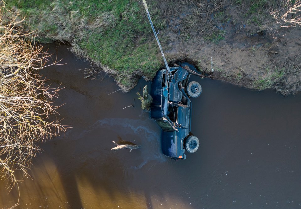A tractor holds the 4×4 by a strap so the vehicle doesn't move any further down the river