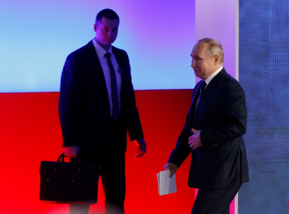 Putin passes his shadowy 'bag man' as he walks out to the stage