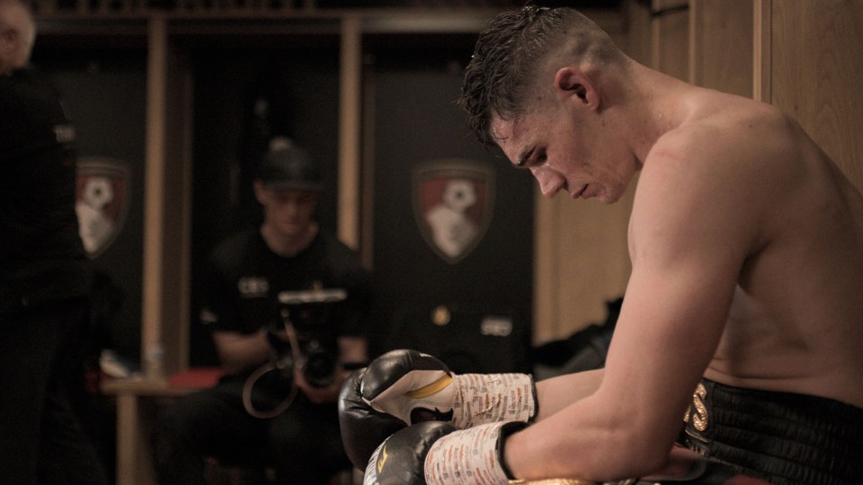 a man wearing boxing gloves sits in a locker room
