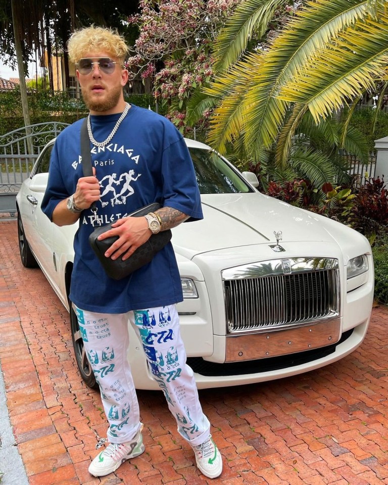 a man wearing a blue balenciaga shirt stands in front of a white car