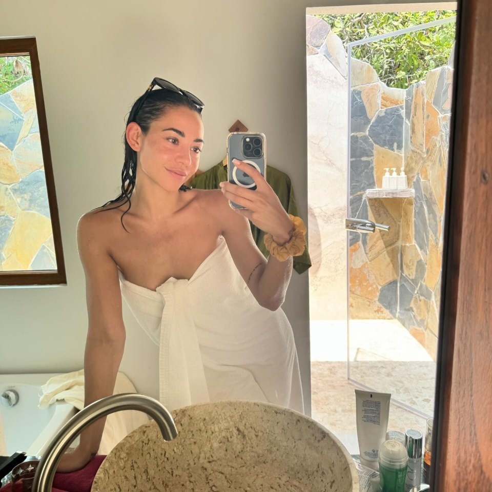 a woman wrapped in a white towel is taking a selfie in a bathroom