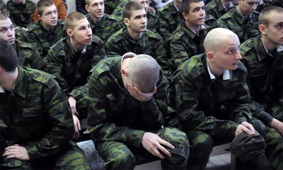 A group of young men in Russian military uniforms, one of whom is sitting with his head in his hands.