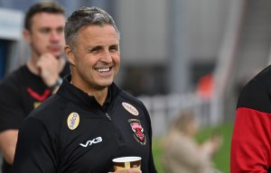 a man wearing a black vx3 jacket holds a cup of coffee