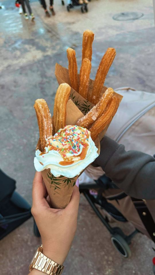 a person holding a cone of churros with whipped cream and sprinkles