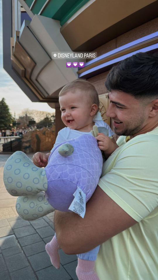 a man is holding a baby in front of a sign that says disneyland paris