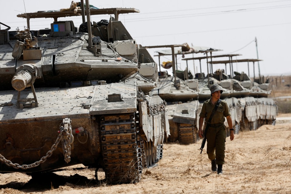An Israeli soldier walks near tanks parked near the southern Gaza border