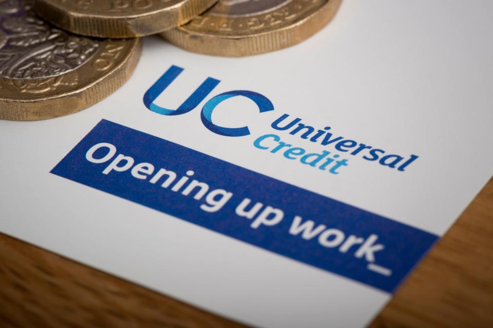 PXEK8K A piece of stationery featuring the Universal Credit logo, rests on a table along with some ¿1 coins.