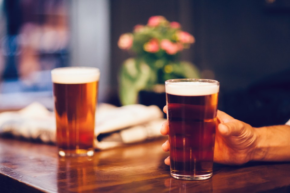 Two pints of beer on wooden table. Humand hand grabs one of them.