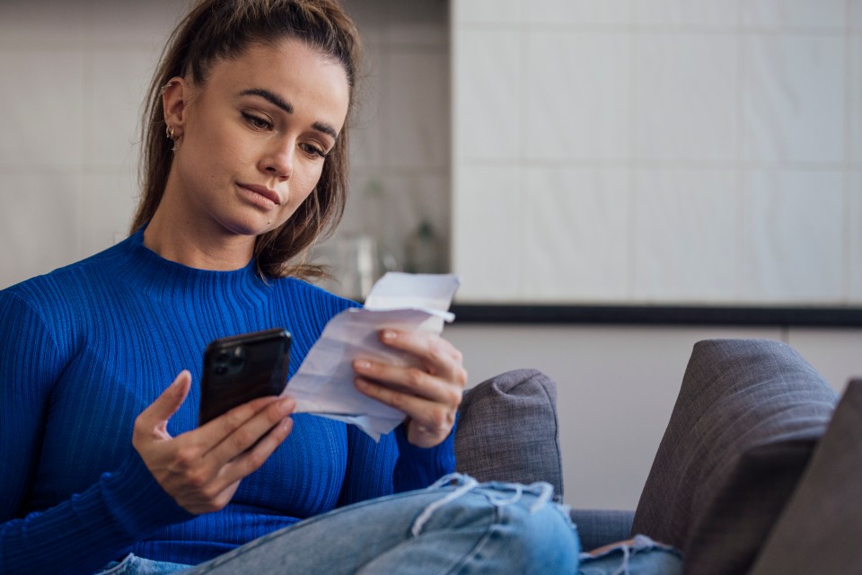 A portrait of a woman sitting at home in Newcastle-Upon-Tyne, England. She has receipts in one hand and her smartphone in the other as she works out her finances.