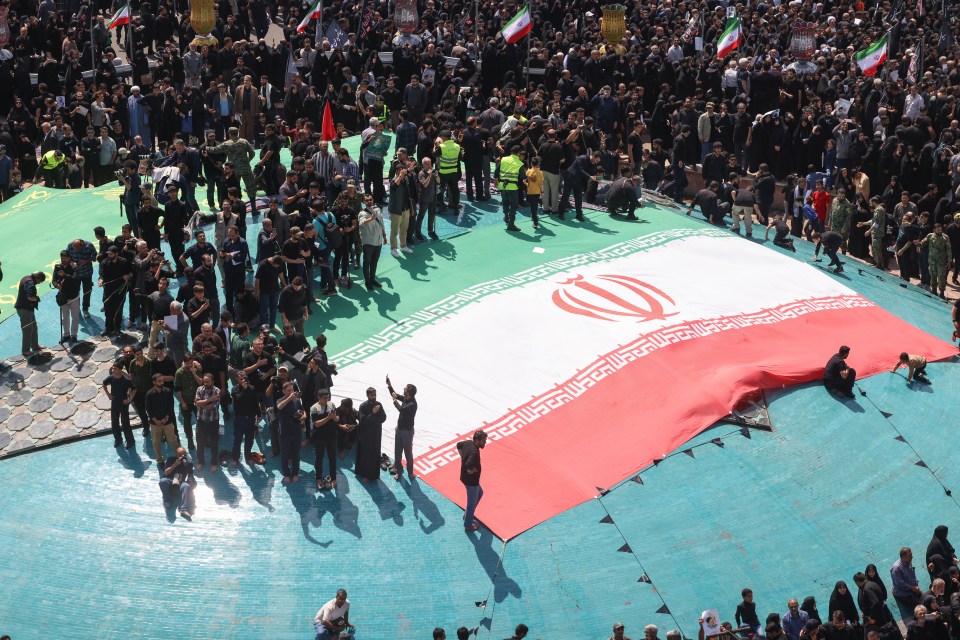 a crowd of people gathered around a large iranian flag