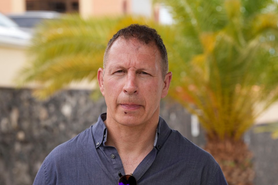 a man wearing sunglasses stands in front of a palm tree