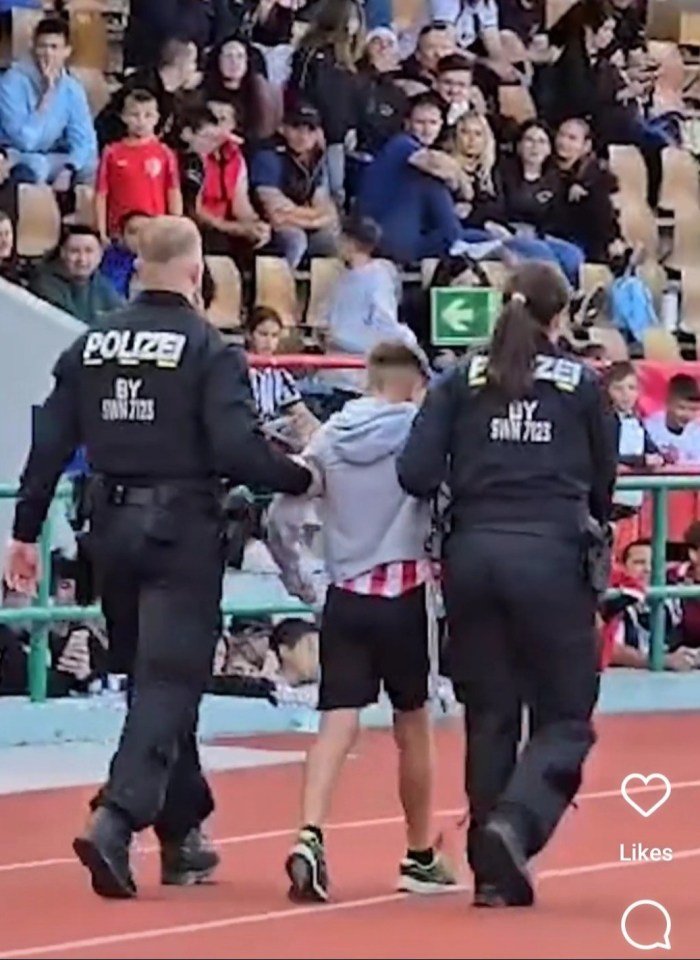 A young fan is escorted off the pitch by police officers after storming the session