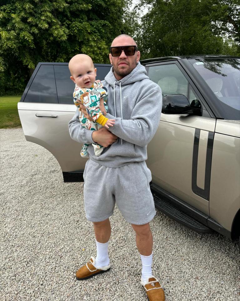 a man holding a baby in front of a range rover