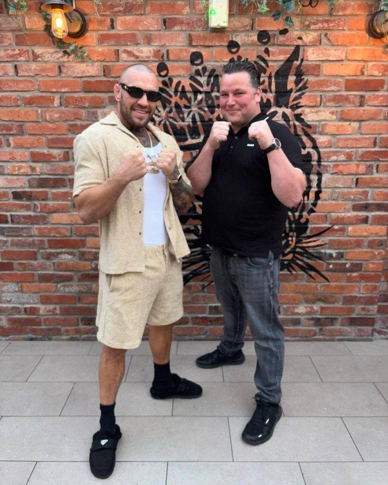 two men are posing for a picture in front of a brick wall