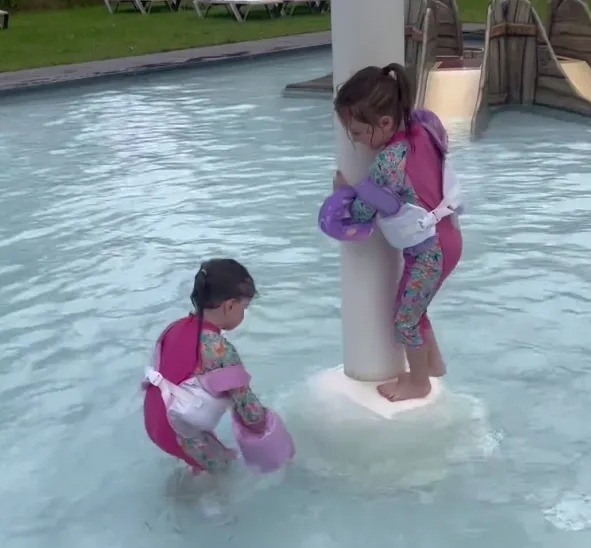 Two toddlers in flotation devices in a pool.