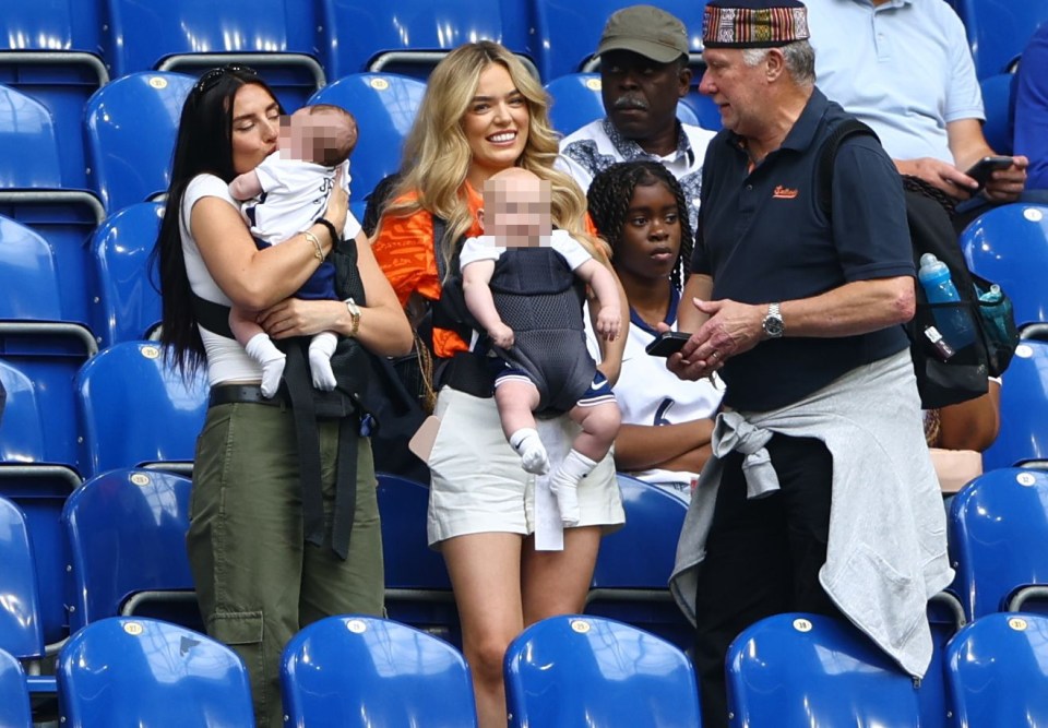 a man wearing a superdry shirt talks to a woman holding a baby