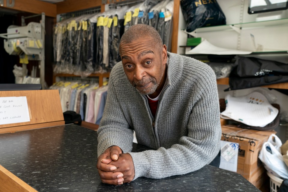 a man in a grey sweater sits at a counter in a dry cleaners