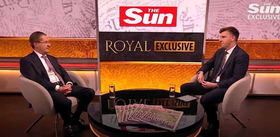 Two men in suits sitting on a talk show set discussing a royal exclusive.