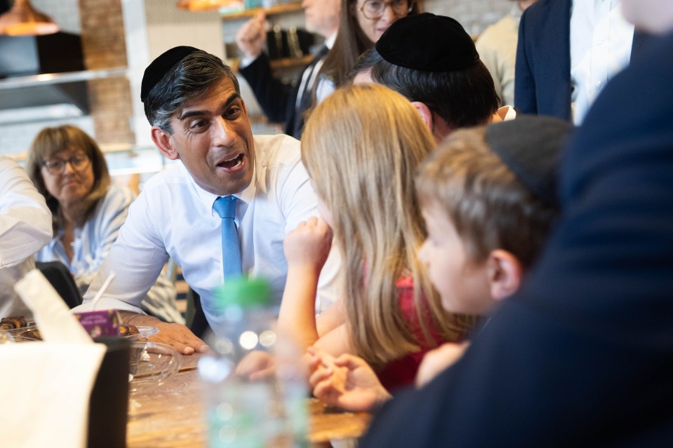 a man wearing a yarmulke talks to a group of children