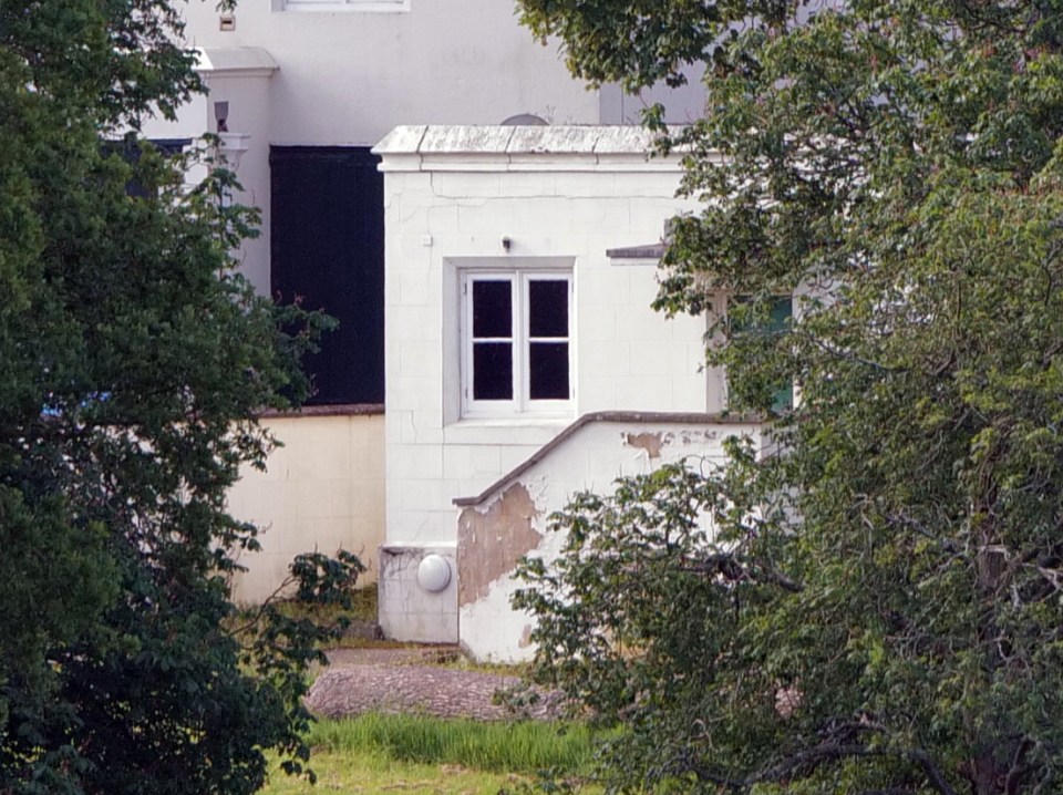 Partial view of a white building undergoing refurbishment, partially obscured by trees.