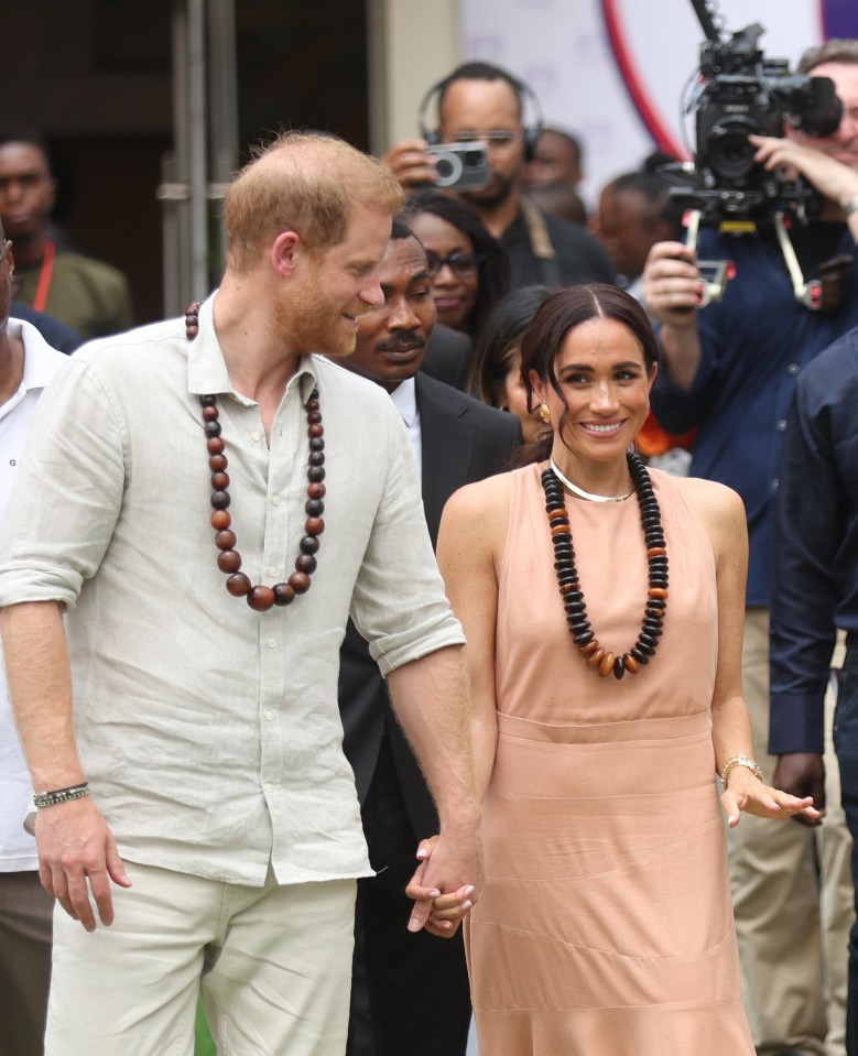 Prince Harry and Meghan Markle holding hands at the Lightway Academy in Abuja, Nigeria.