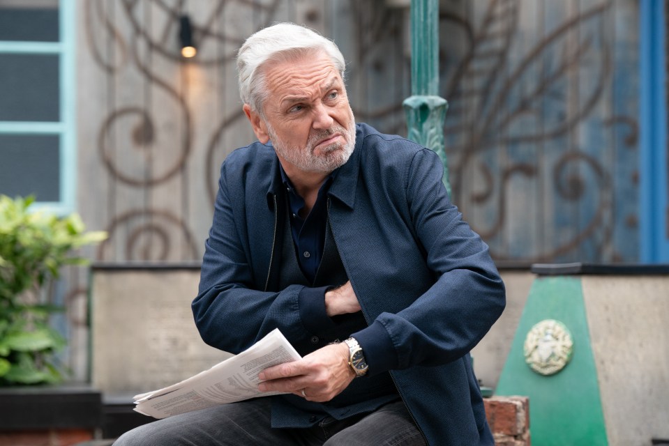 Rocky from EastEnders looking thoughtfully at a newspaper.