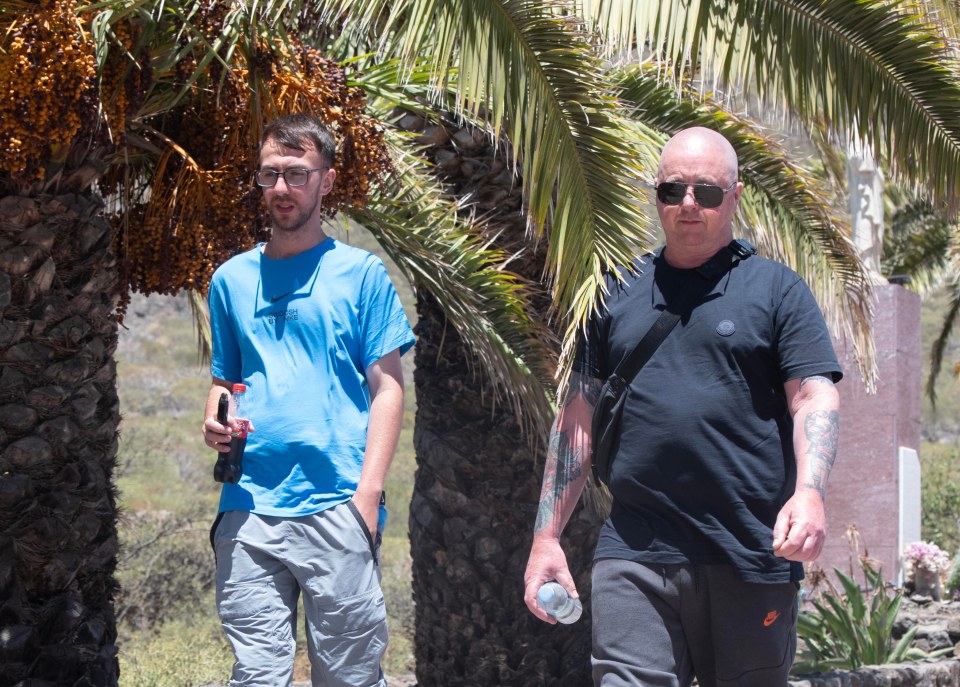 two men walking in front of a palm tree with one wearing a nike shirt