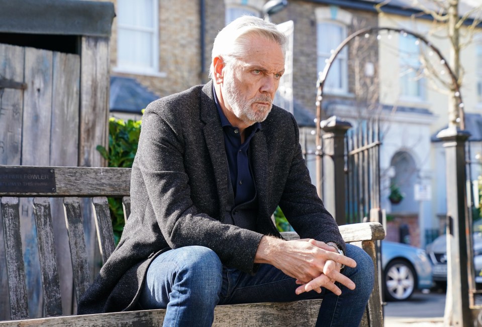 A man sits on a park bench, looking pensive.