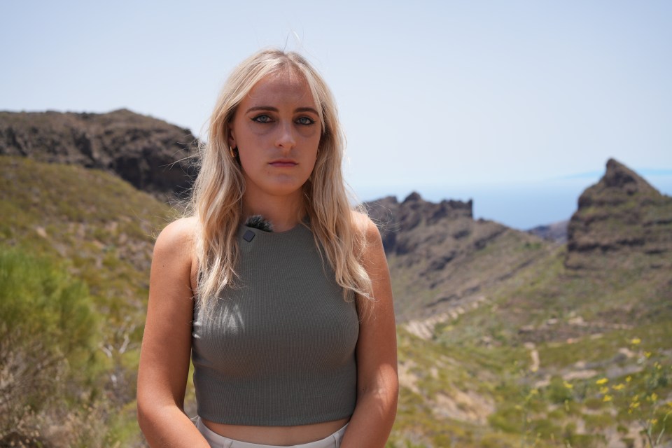 a woman in a crop top stands in front of a mountain