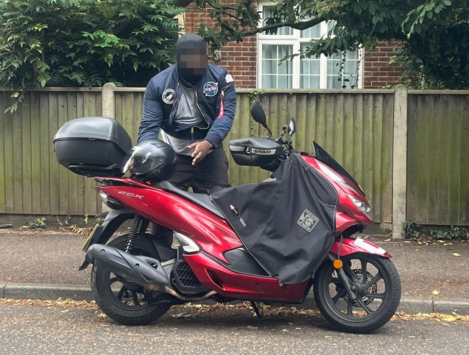 a man wearing a nasa jacket sits on a red scooter