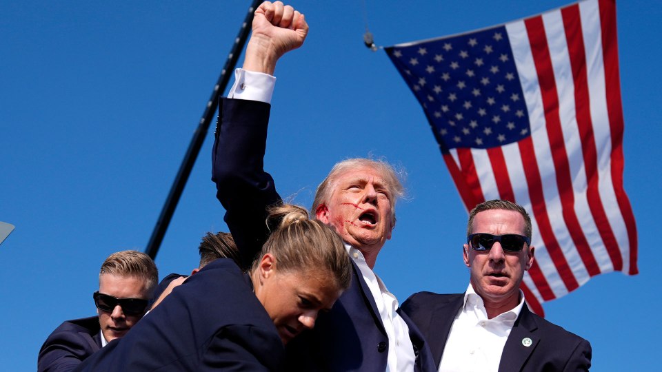 a man in a suit holds up his fist in front of an american flag