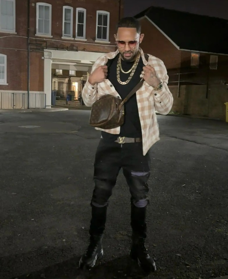 a man with a louis vuitton bag on his shoulder stands in front of a brick building