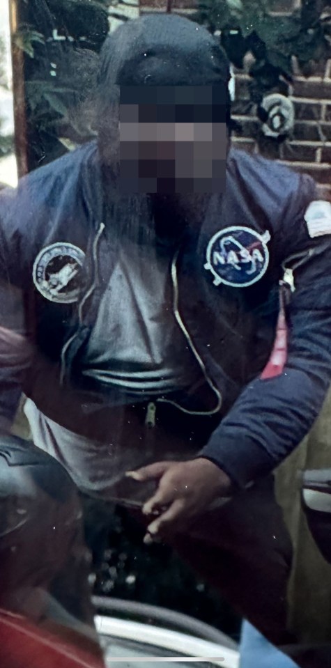 a man wearing a nasa jacket stands in front of a brick wall